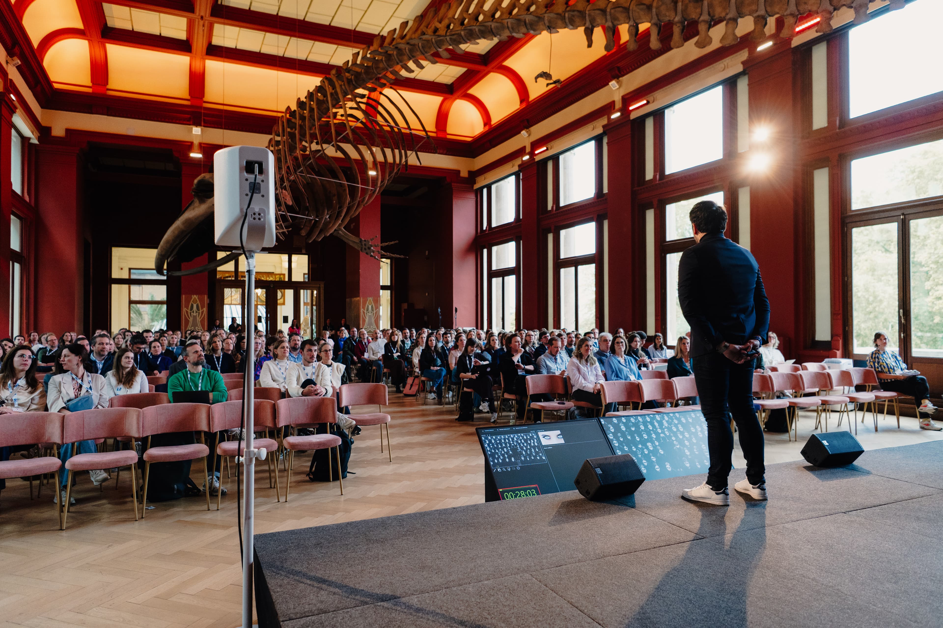 Henny Speelman op het podium tijdens een keynote, met de zaal en publiek in beeld
